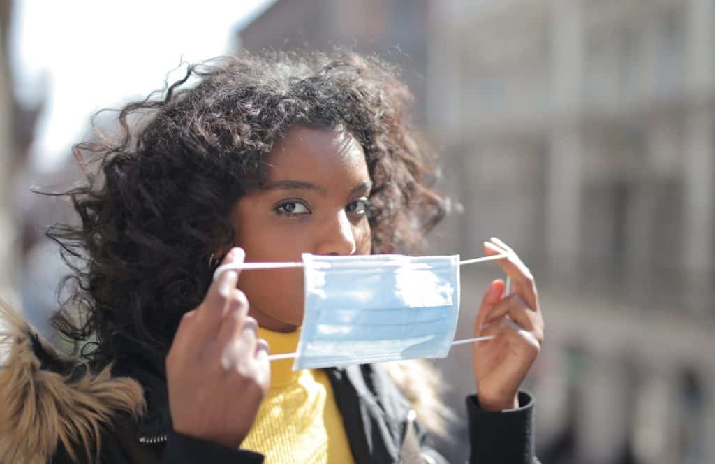 focused young ethnic lady putting on medical mask on street 3960922